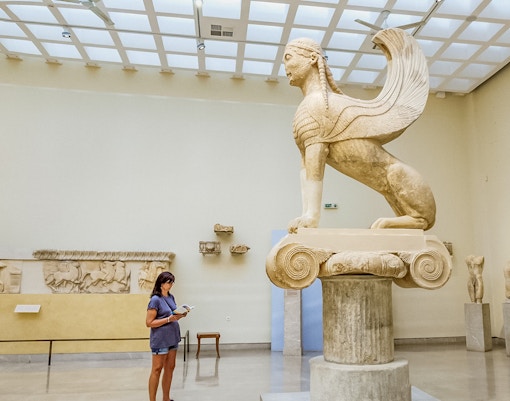 Tourist using audio guide near Sphinx statue in Delphi Museum, Greece.
