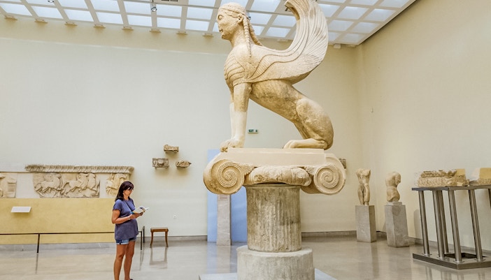 Tourist using audio guide near Sphinx statue in Delphi Museum, Greece.