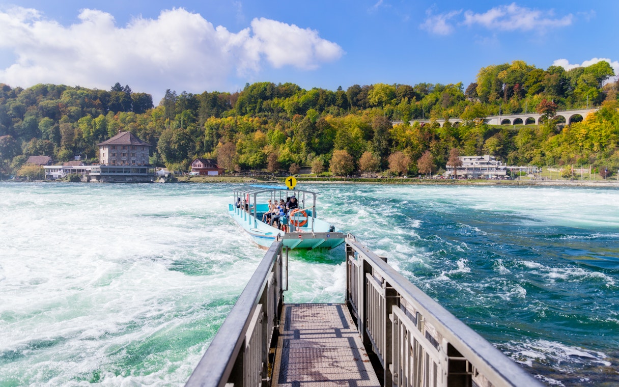 Boat approaching dock at Rhine Falls with passengers, surrounded by lush greenery.