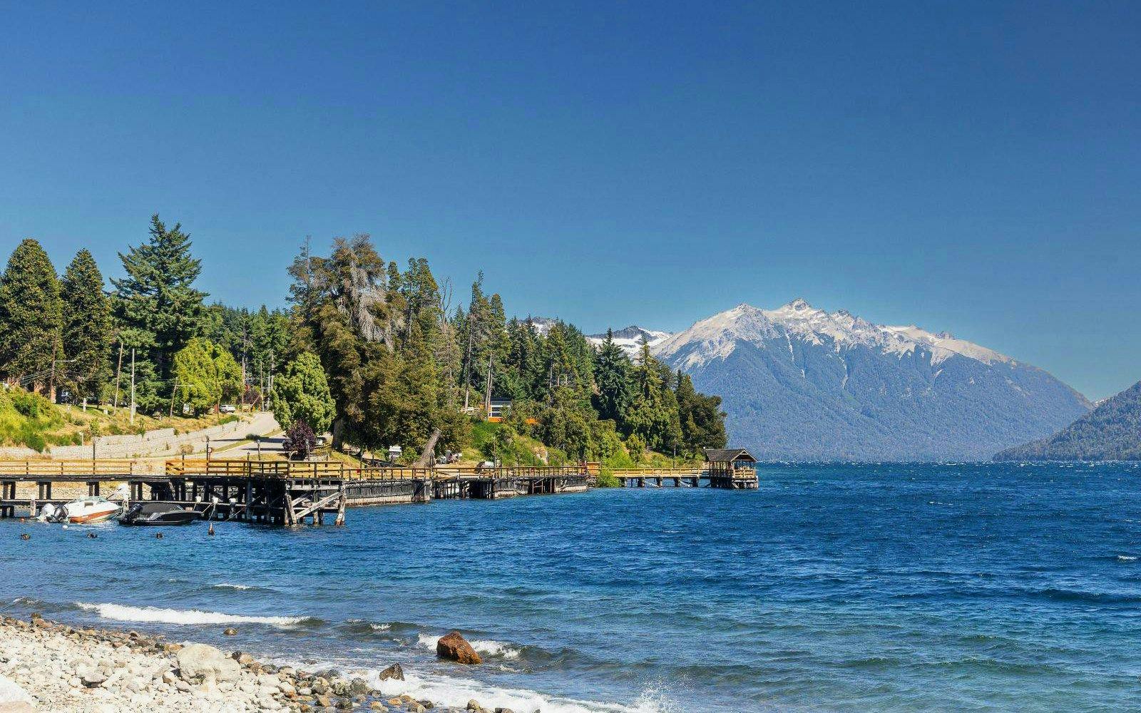 Lakeside beach with clear water, mountain views, and dock near Villa Traful.