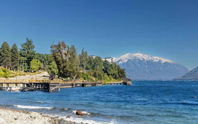 Lakeside beach with clear water, mountain views, and dock near Villa Traful.