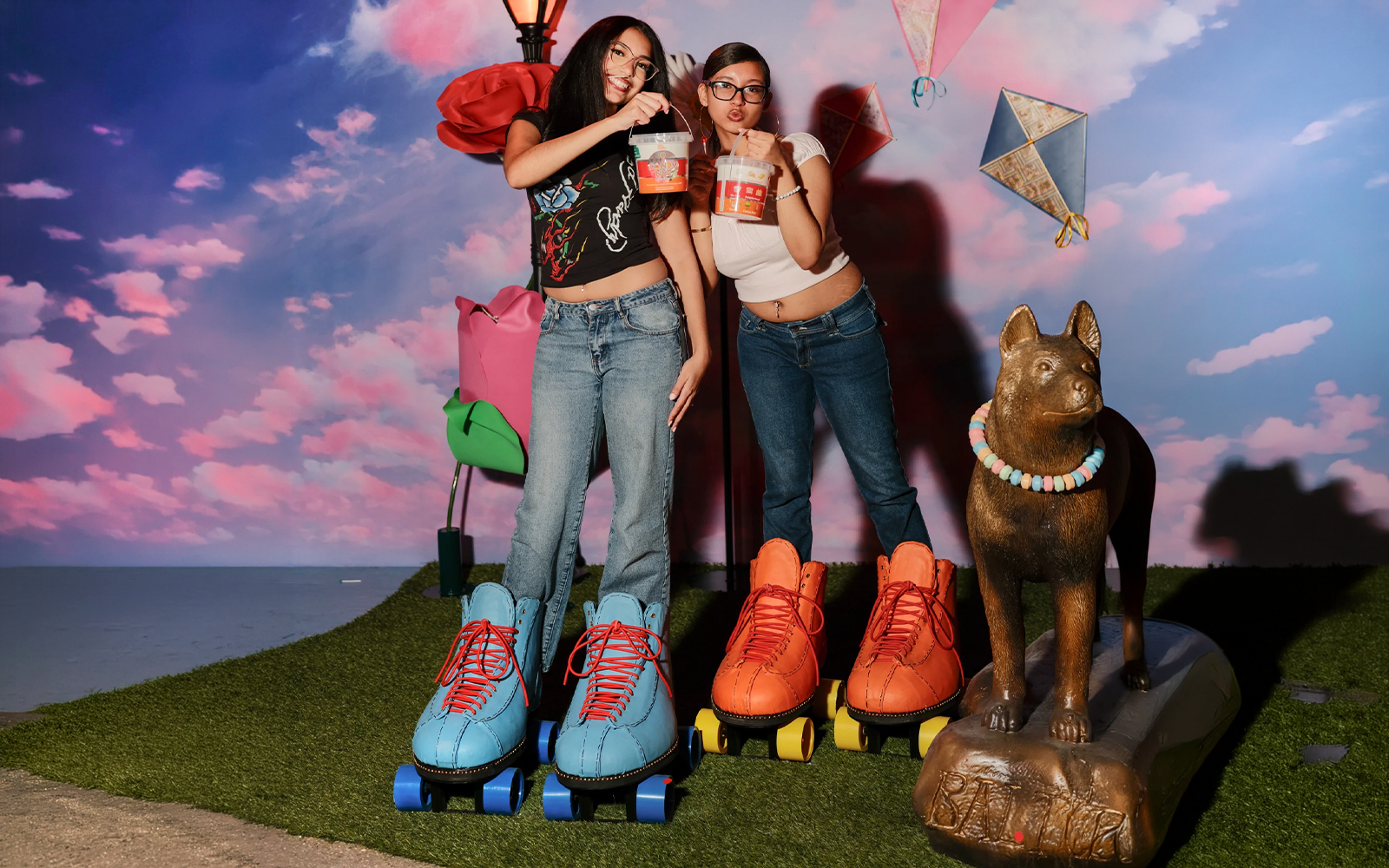 Two people enjoying the iCandy Experience in NYC with oversized roller skates and a candy necklace statue.