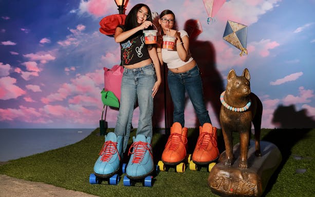 Two people enjoying the iCandy Experience in NYC with oversized roller skates and a candy necklace statue.
