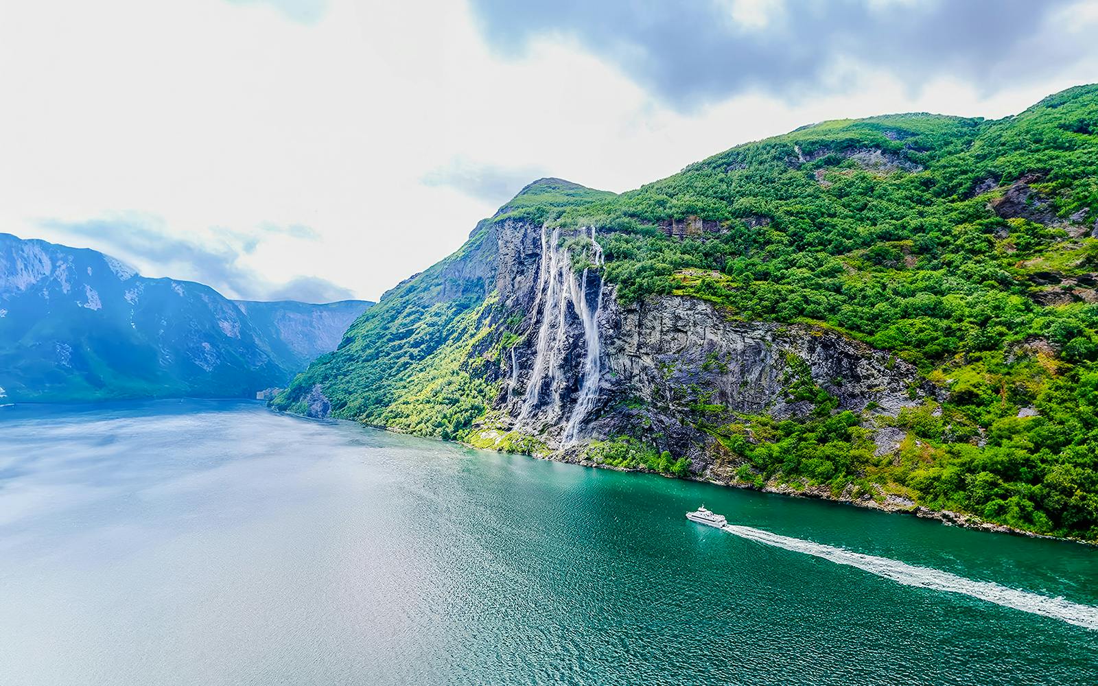 Boat cruising near waterfall in Geiranger Fjord, Norway.