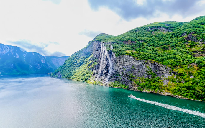 Boat cruising near waterfall in Geiranger Fjord, Norway.