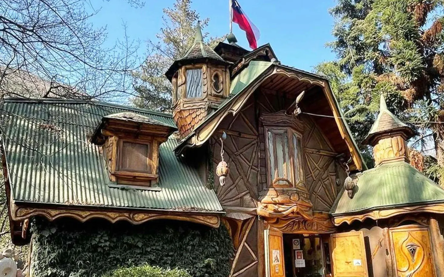 Rustic wooden cabin with green roof in Cajon del Maipo, Santiago, surrounded by trees.