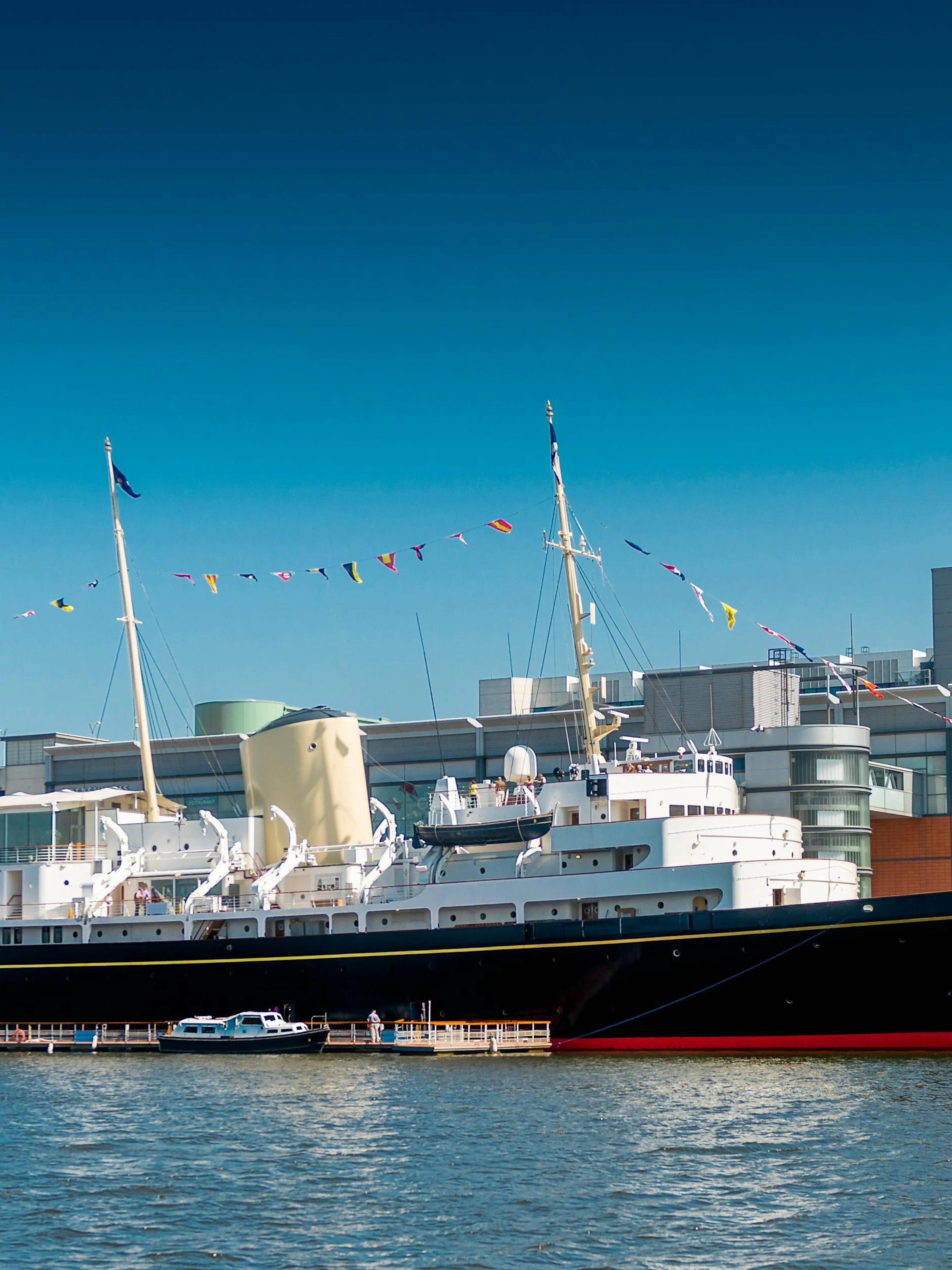 Royal Yacht Britannia docked in Edinburgh with colorful flags.