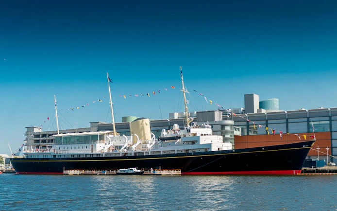 Royal Yacht Britannia docked in Edinburgh with colorful flags.