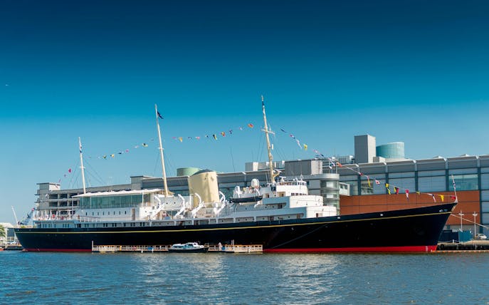 Royal Yacht Britannia docked in Edinburgh with colorful flags.