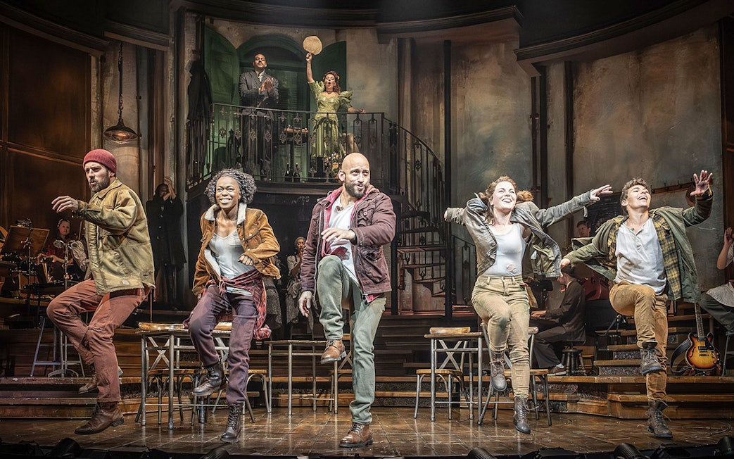 Performers dancing energetically on stage during a Hadestown musical scene.
