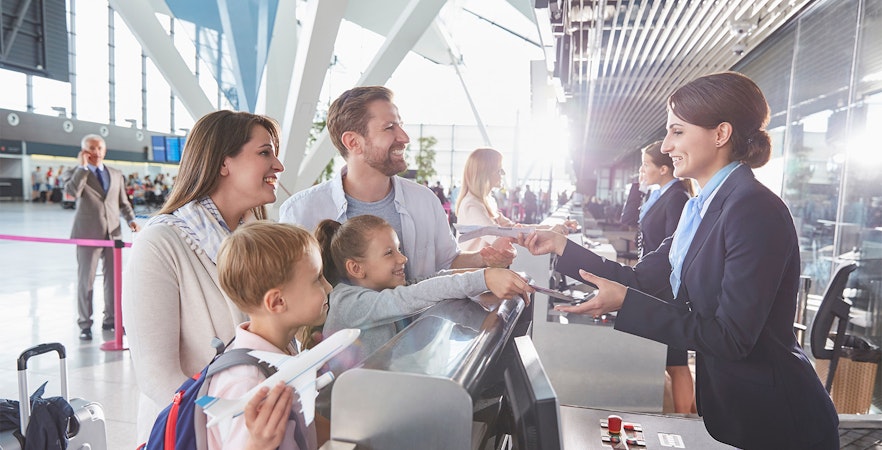 Family checking in at Rome airport counter, smiling and handing over passports.