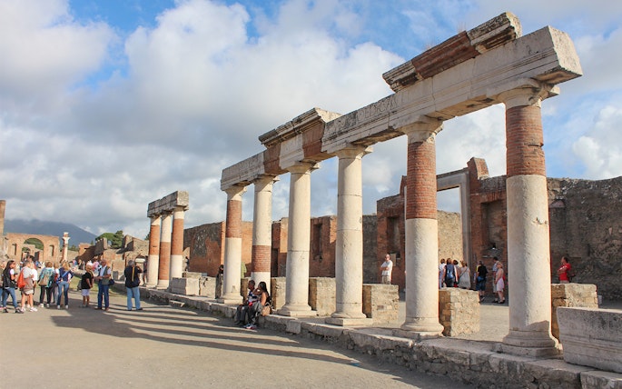 Ancient ruins with columns in Pompeii, Italy, with tourists exploring the site.