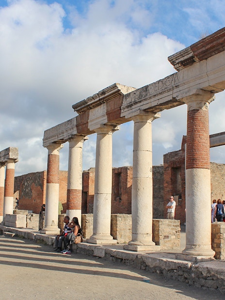 Ancient ruins with columns in Pompeii, Italy, with tourists exploring the site.