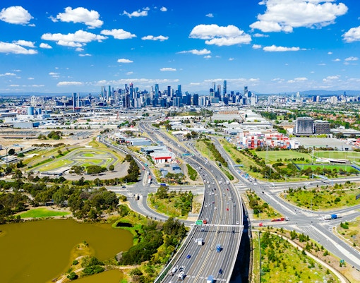 Aerial view of Melbourne skyline with highways and green spaces in the foreground.