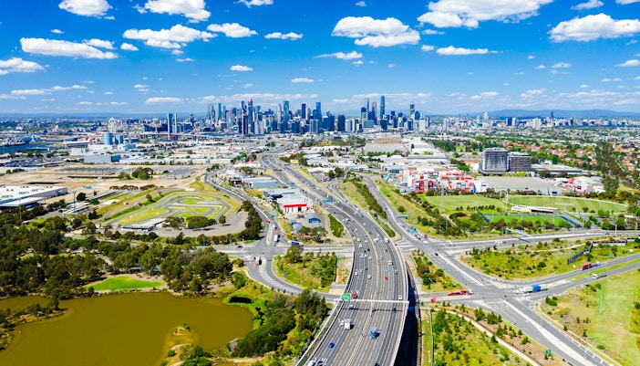 Aerial view of Melbourne skyline with highways and green spaces in the foreground.