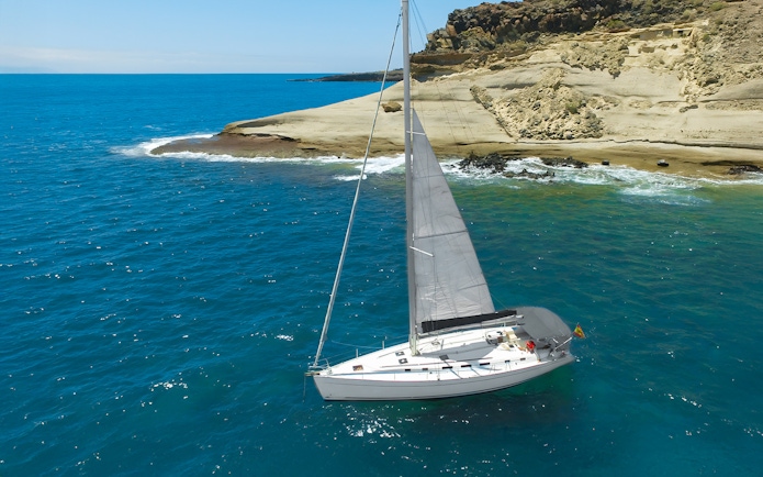 Sailboat cruising near rocky coastline in Tenerife for whale and dolphin watching.