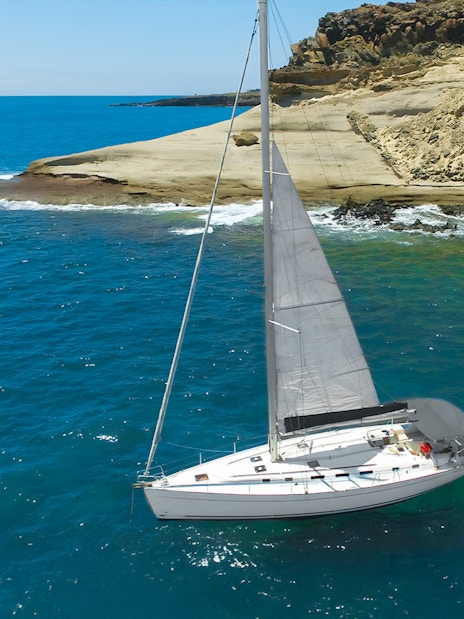 Sailboat cruising near rocky coastline in Tenerife for whale and dolphin watching.