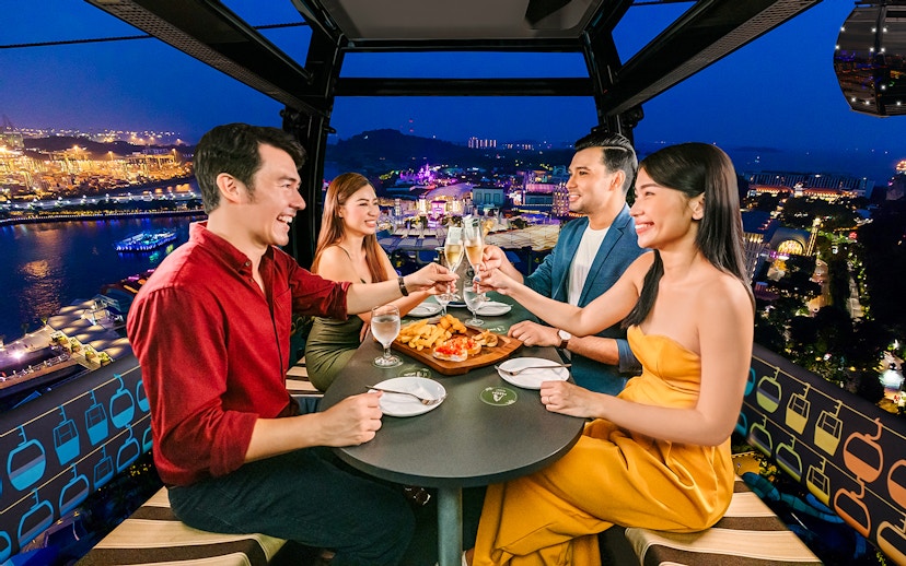 Four guests enjoying a meal in a Singapore cable car with city lights in the background.