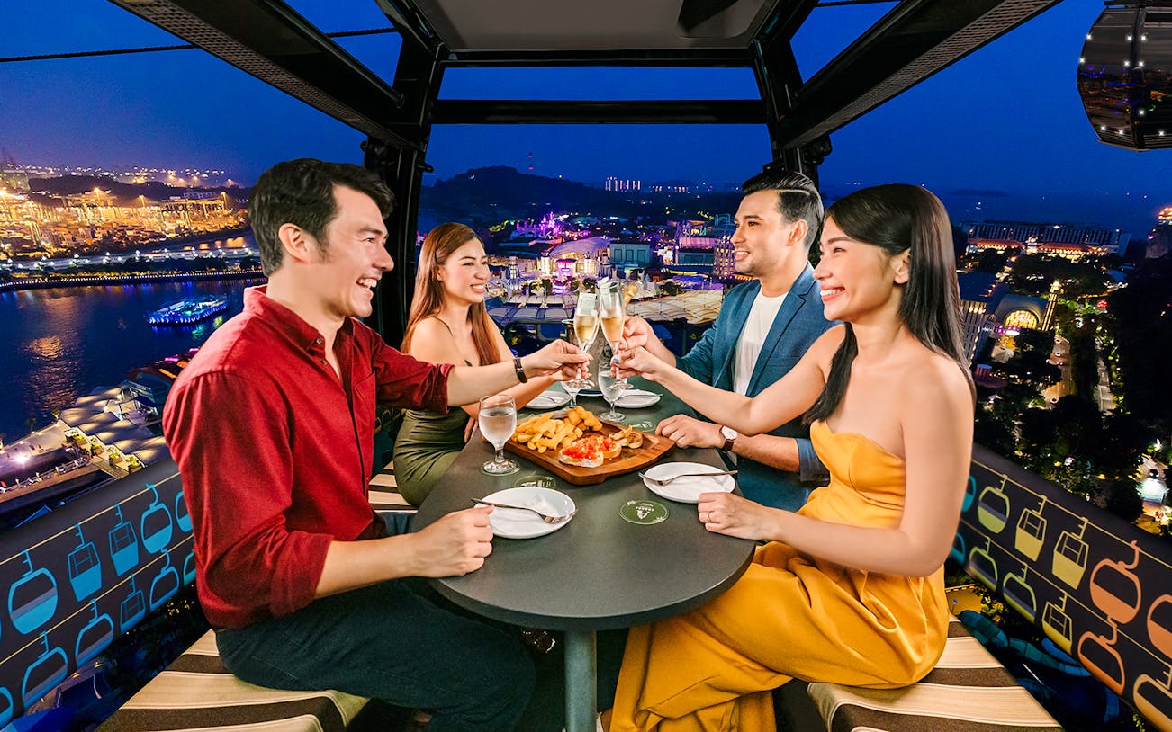 Four guests enjoying a meal in a Singapore cable car with city lights in the background.