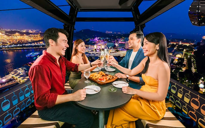 Four guests enjoying a meal in a Singapore cable car with city lights in the background.