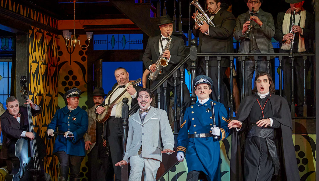 Performers in a lively scene from "The Barber of Seville" opera, featuring musicians and actors in period costumes.