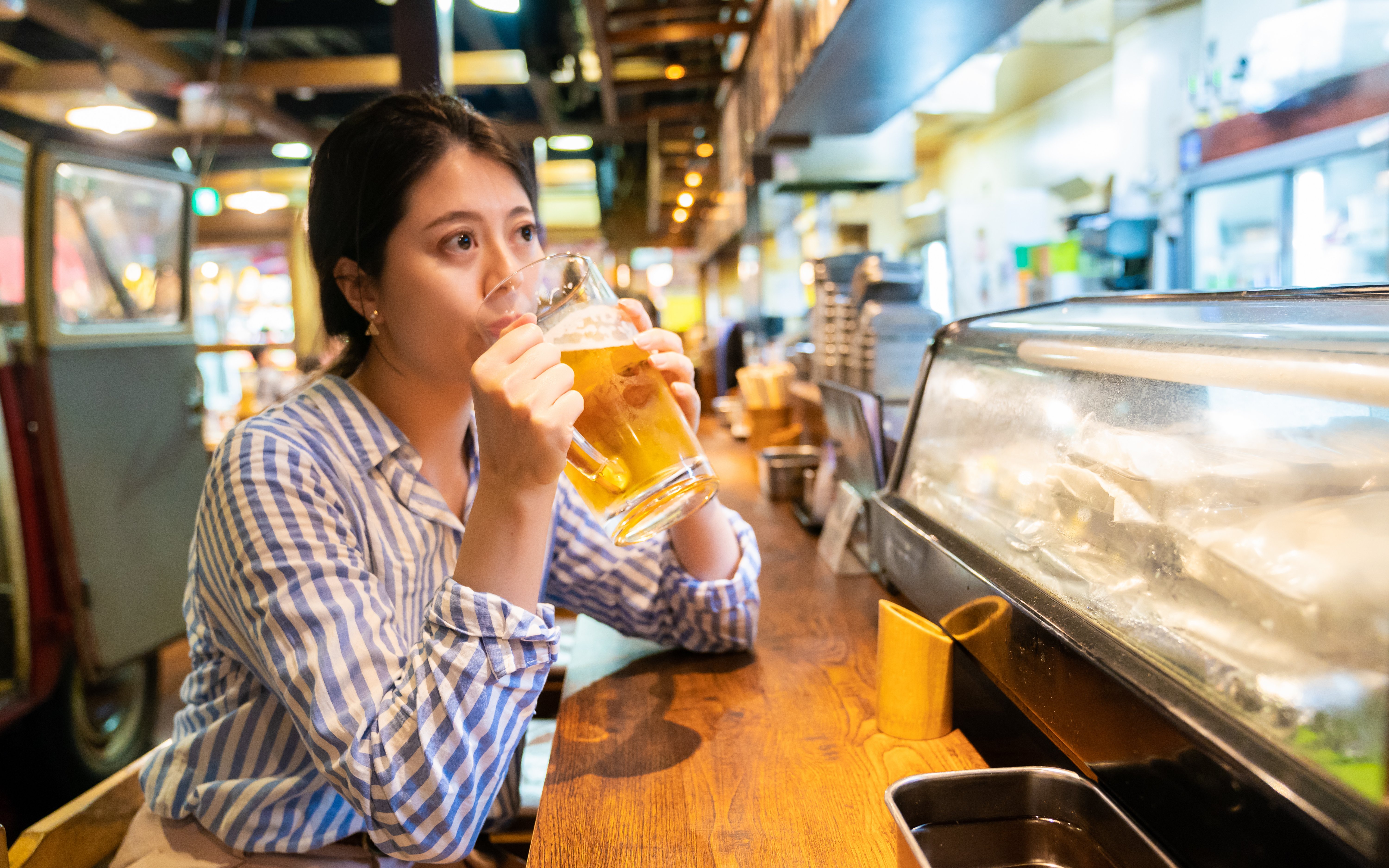 Asian woman enjoying a drink at an izakaya counter in Japan.