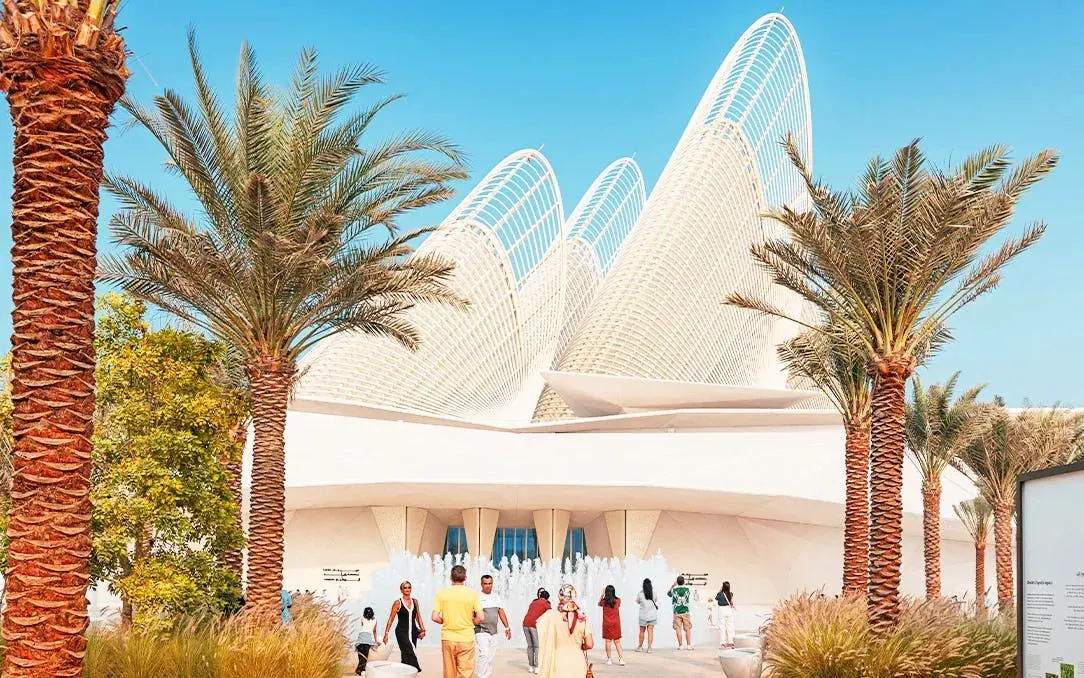 Visitors at Zayed National Museum entrance, Abu Dhabi, with palm trees and unique architecture.