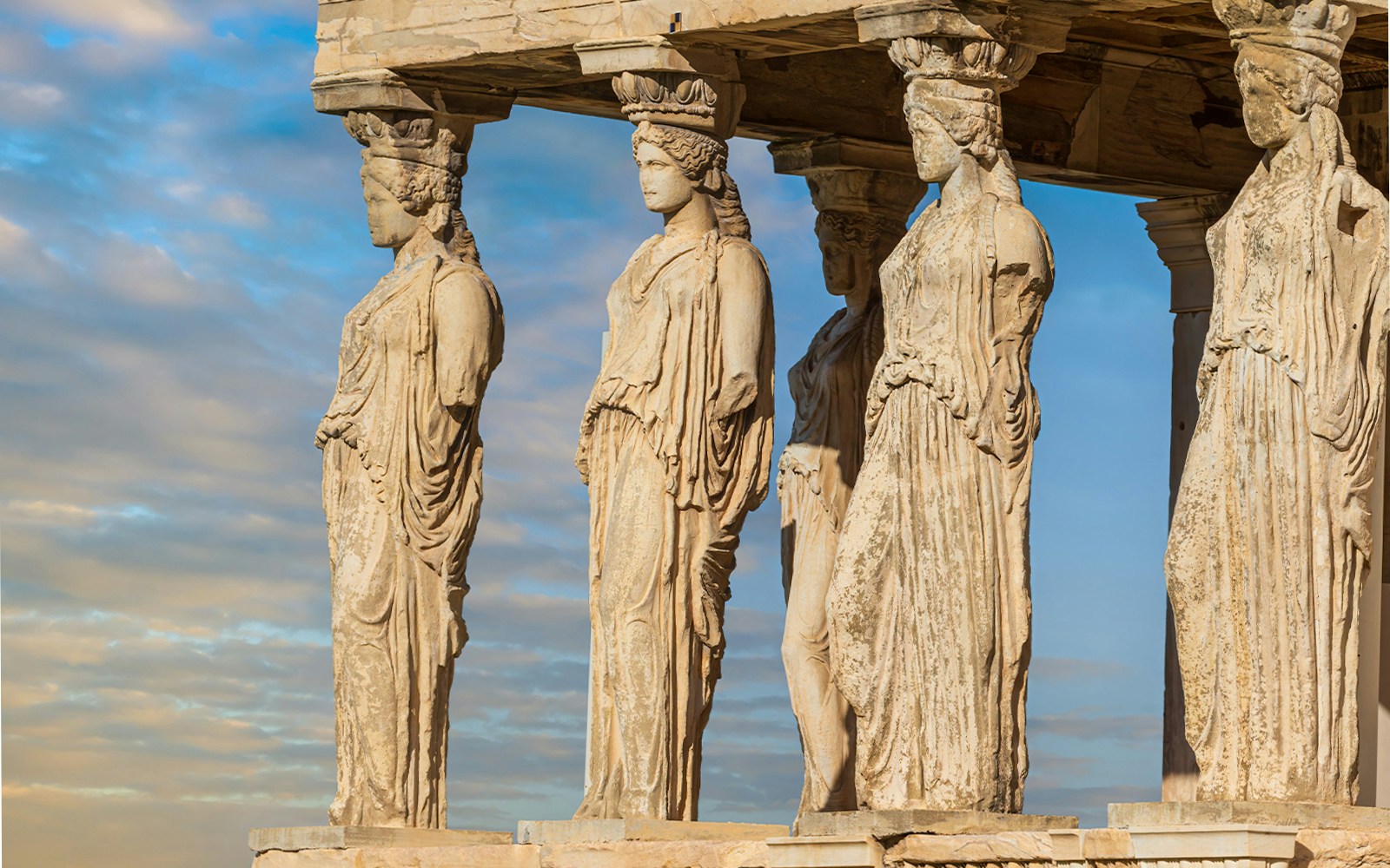 Caryatids of the Erechtheion temple in Athens, Greece, under a blue sky.