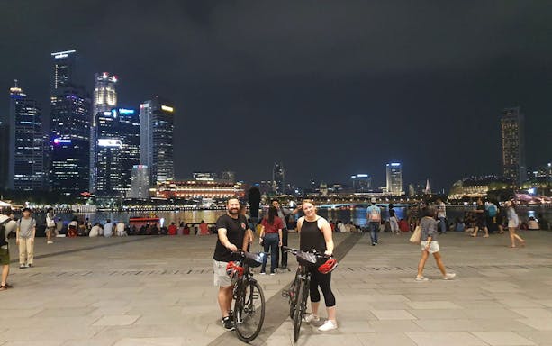 Cyclists at Marina Bay waterfront during night bike tour, Singapore skyline in background.