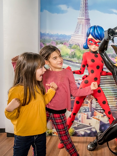 Visitors posing with Ladybug and Cat Noir figures at Grevin Museum, Paris.