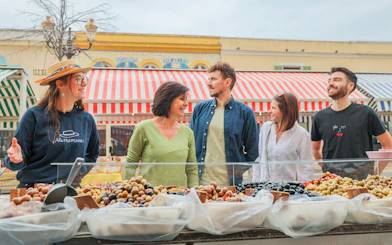 Tour group exploring a market in Nice with a guide, featuring colorful stalls and local produce.