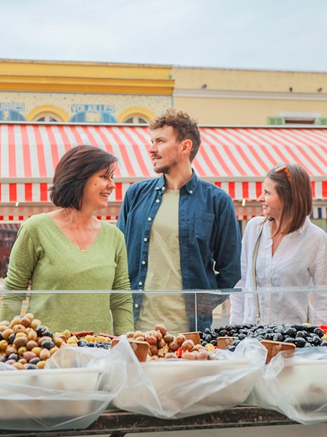 Tour group exploring a market in Nice with a guide, featuring colorful stalls and local produce.
