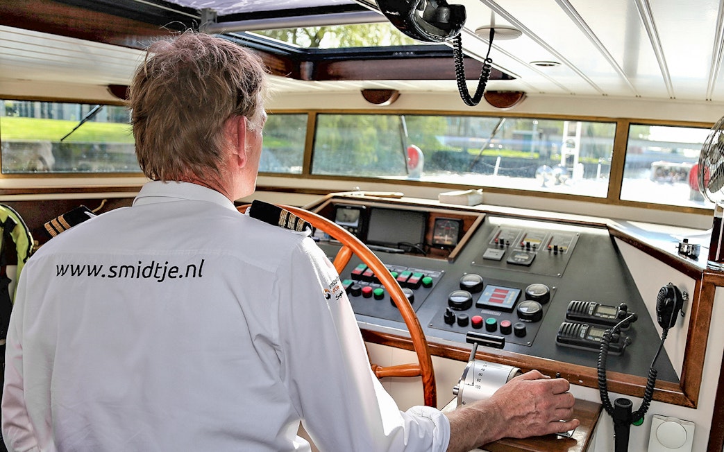 Captain steering a boat on an Amsterdam canal cruise.