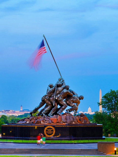 US Marine Corps War Memorial at dusk with Washington Monument in background.