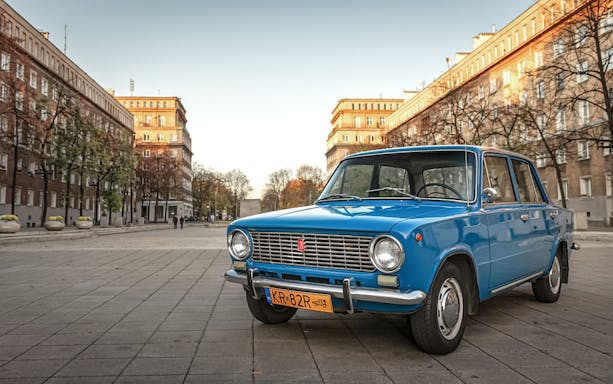 Retro blue car parked in Nowa Huta district, Kraków, with historic buildings in the background.