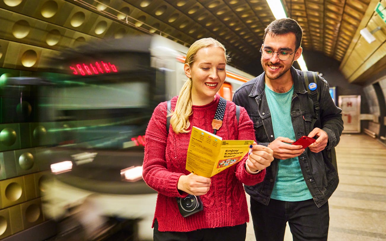 Tourists reading a Prague Visitor Pass in a metro station.