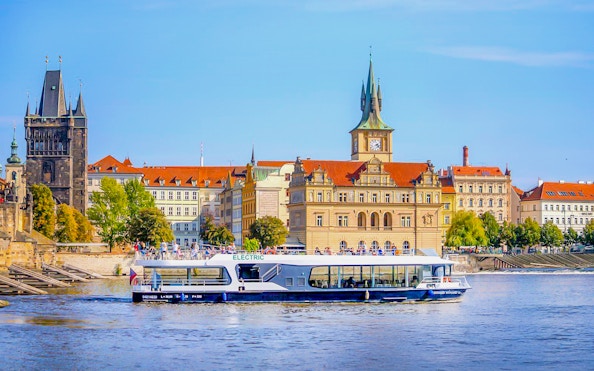 Electric boat cruising on Vltava River with Prague's historic buildings in the background.
