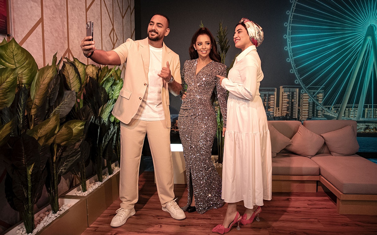 Guests taking a selfie with a wax figure at Madame Tussauds Dubai, with Ain Dubai in the background.