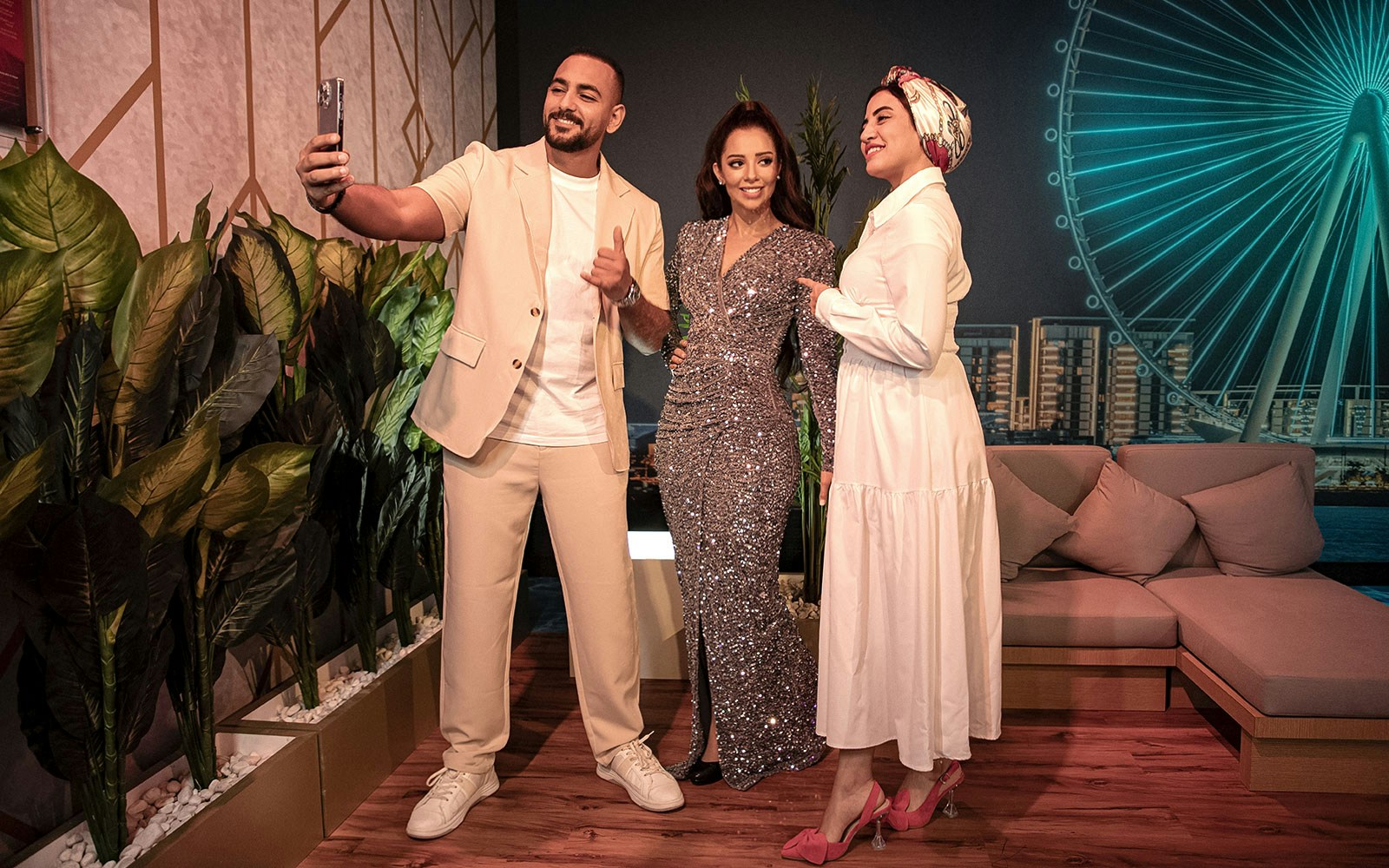 Guests taking a selfie with a wax figure at Madame Tussauds Dubai, with Ain Dubai in the background.