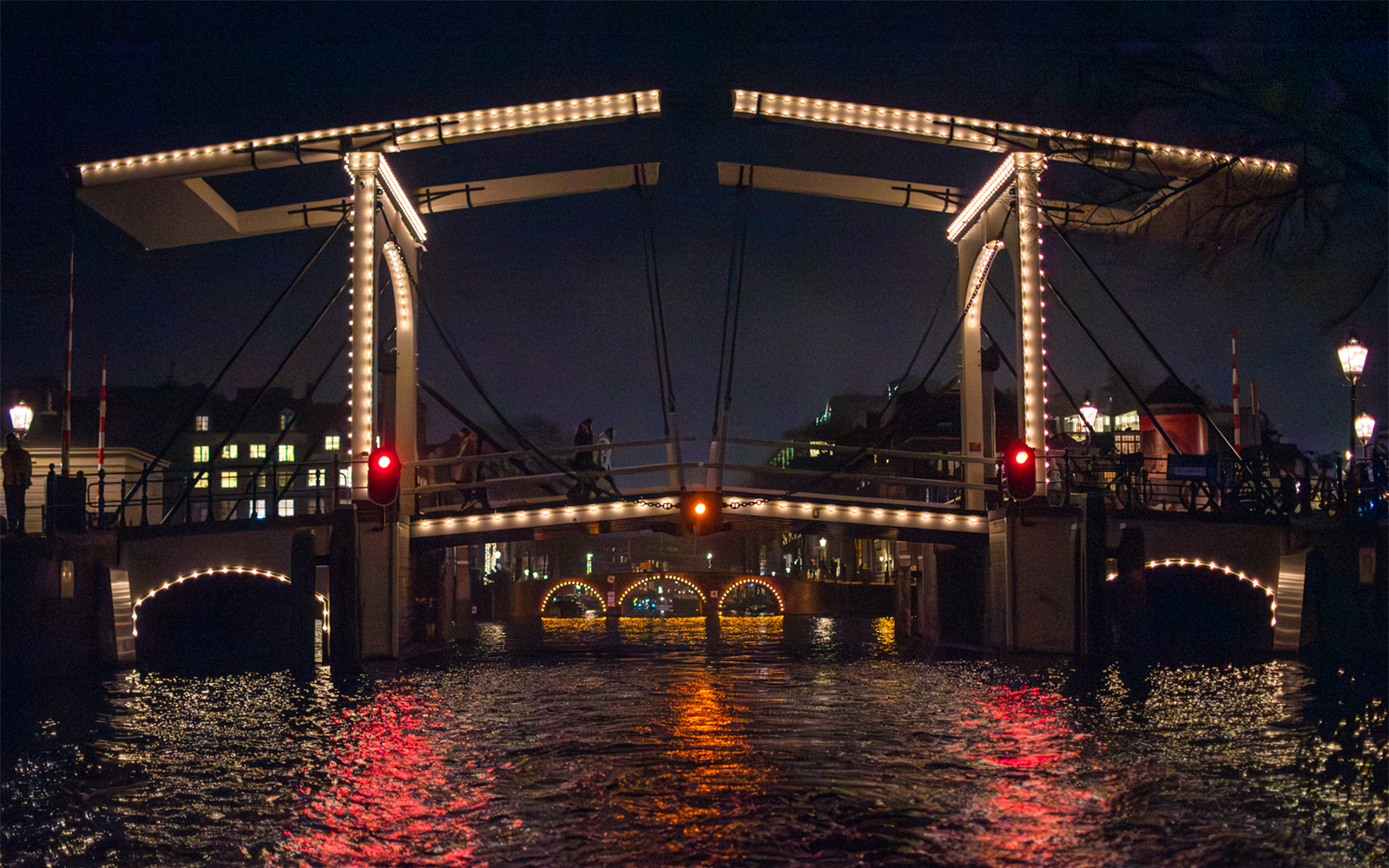 Illuminated bridge over canal during Amsterdam Light Festival cruise.