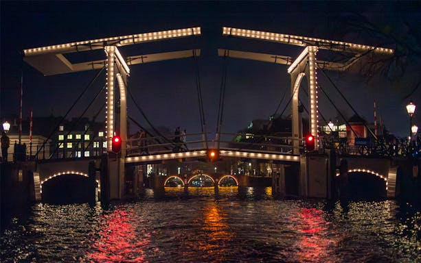Illuminated bridge over canal during Amsterdam Light Festival cruise.