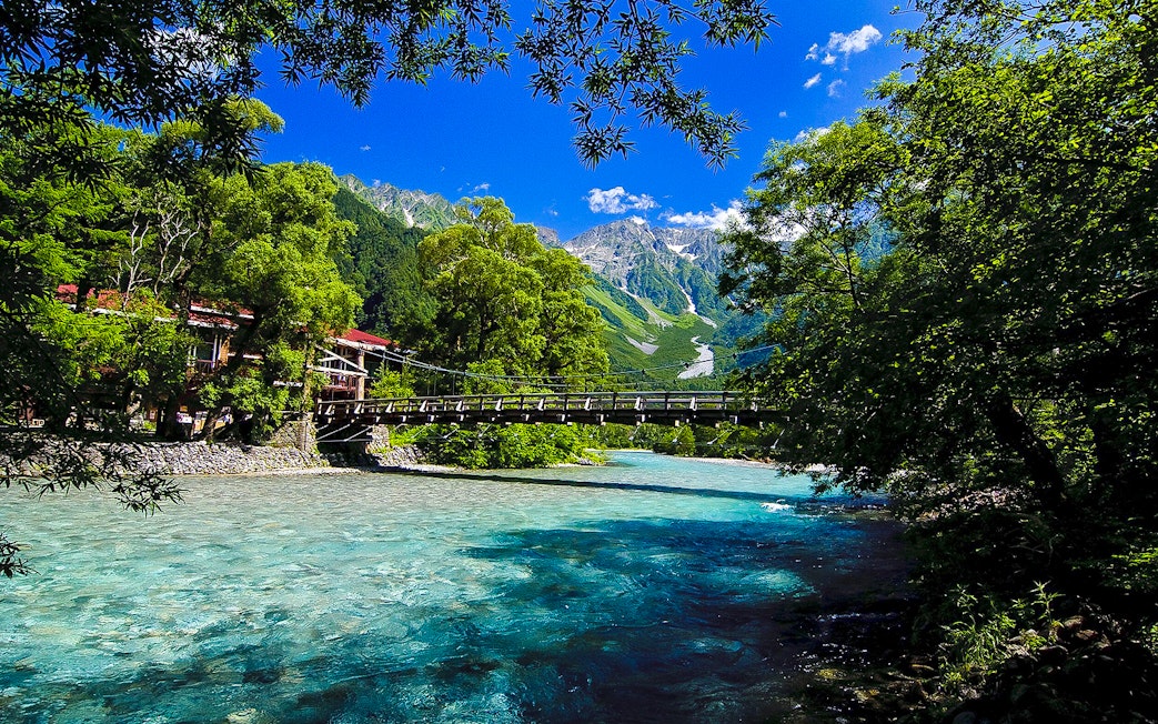 Bridge over clear river with mountain backdrop in Nagano, Japan.