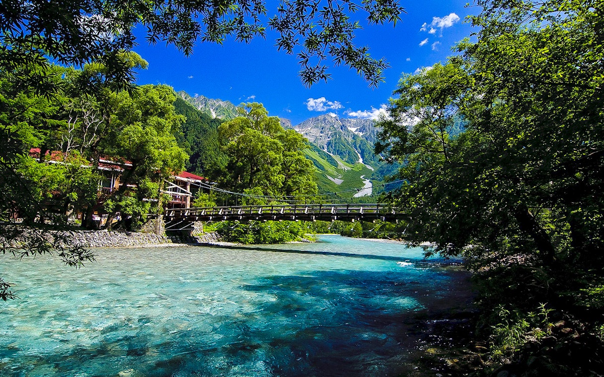 Bridge over clear river with mountain backdrop in Nagano, Japan.