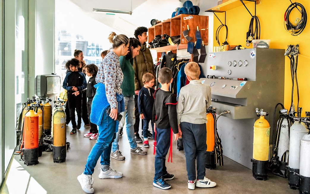 Visitors exploring diving equipment at Cosquer Cave exhibit in Marseille.