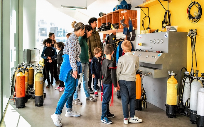 Visitors exploring diving equipment at Cosquer Cave exhibit in Marseille.