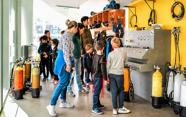 Visitors exploring diving equipment at Cosquer Cave exhibit in Marseille.