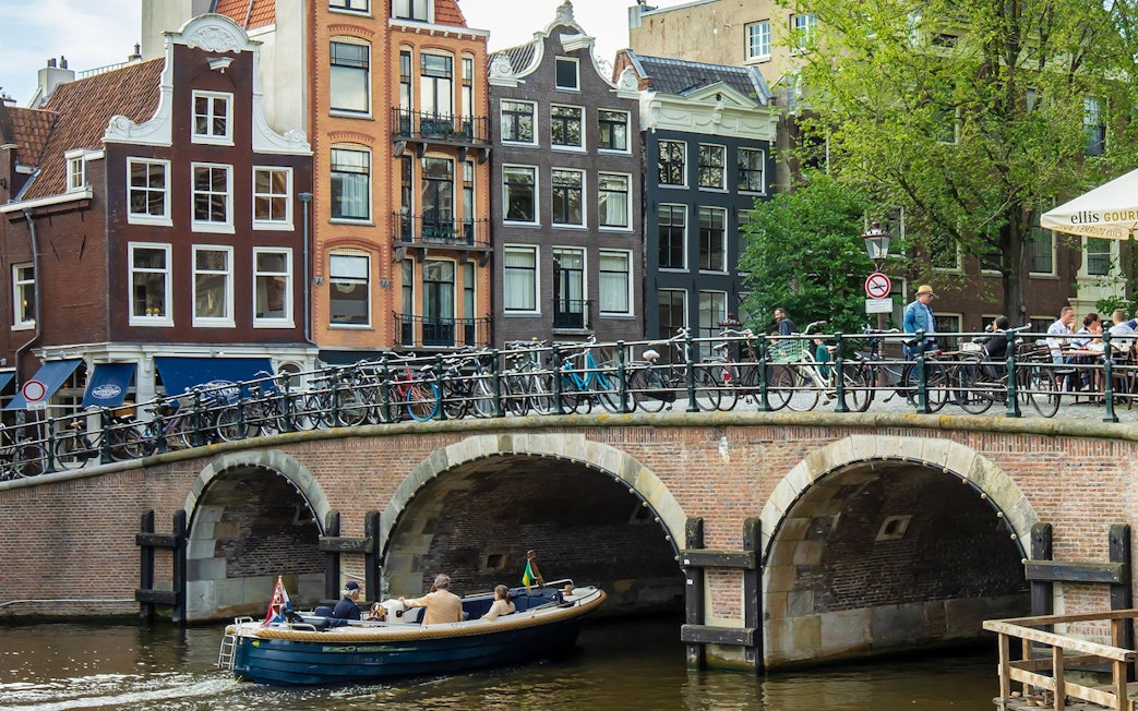 Canal bridge with bicycles and people in Amsterdam, featuring traditional Dutch houses.