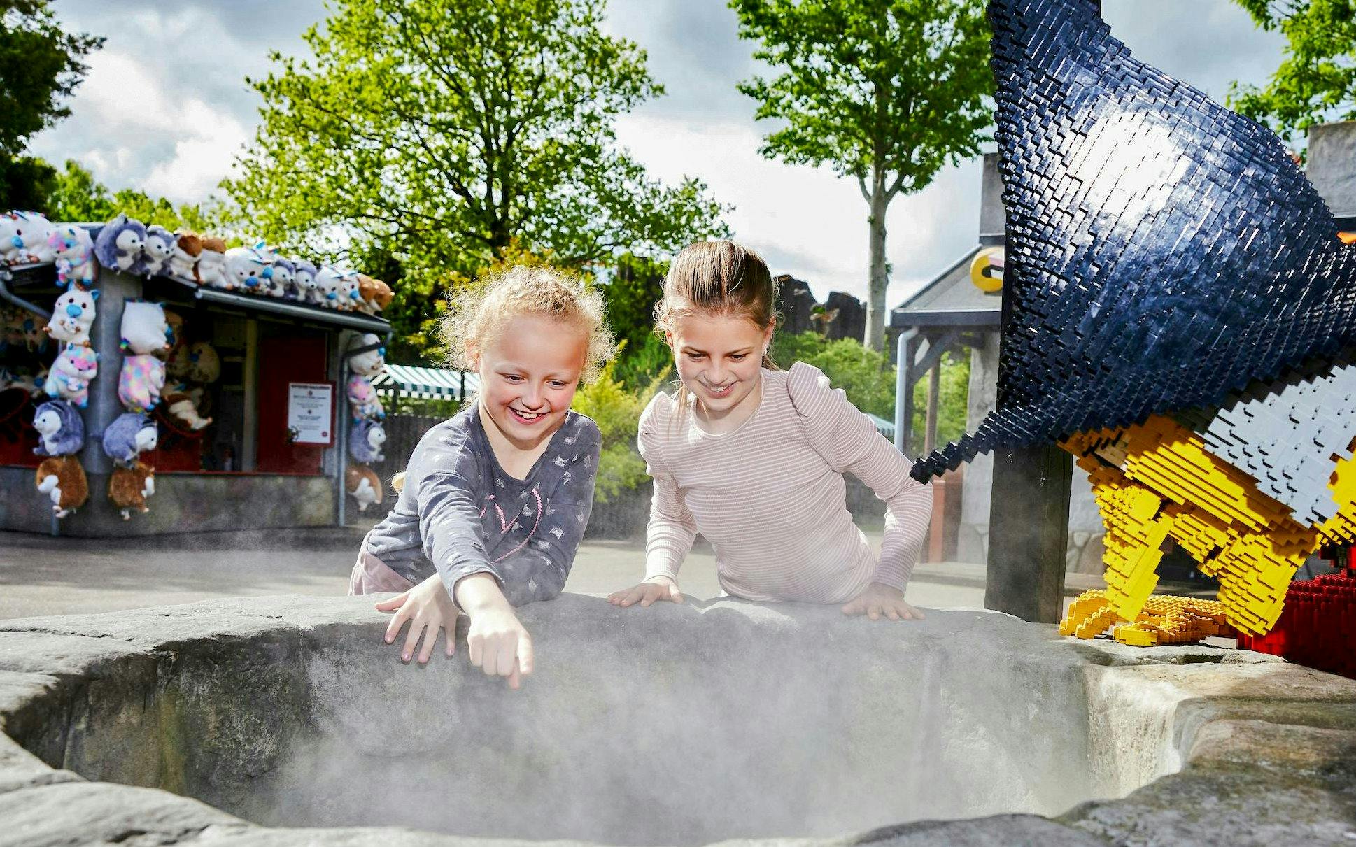 Children exploring a misty well at LEGOLAND® Billund with LEGO sculptures nearby.