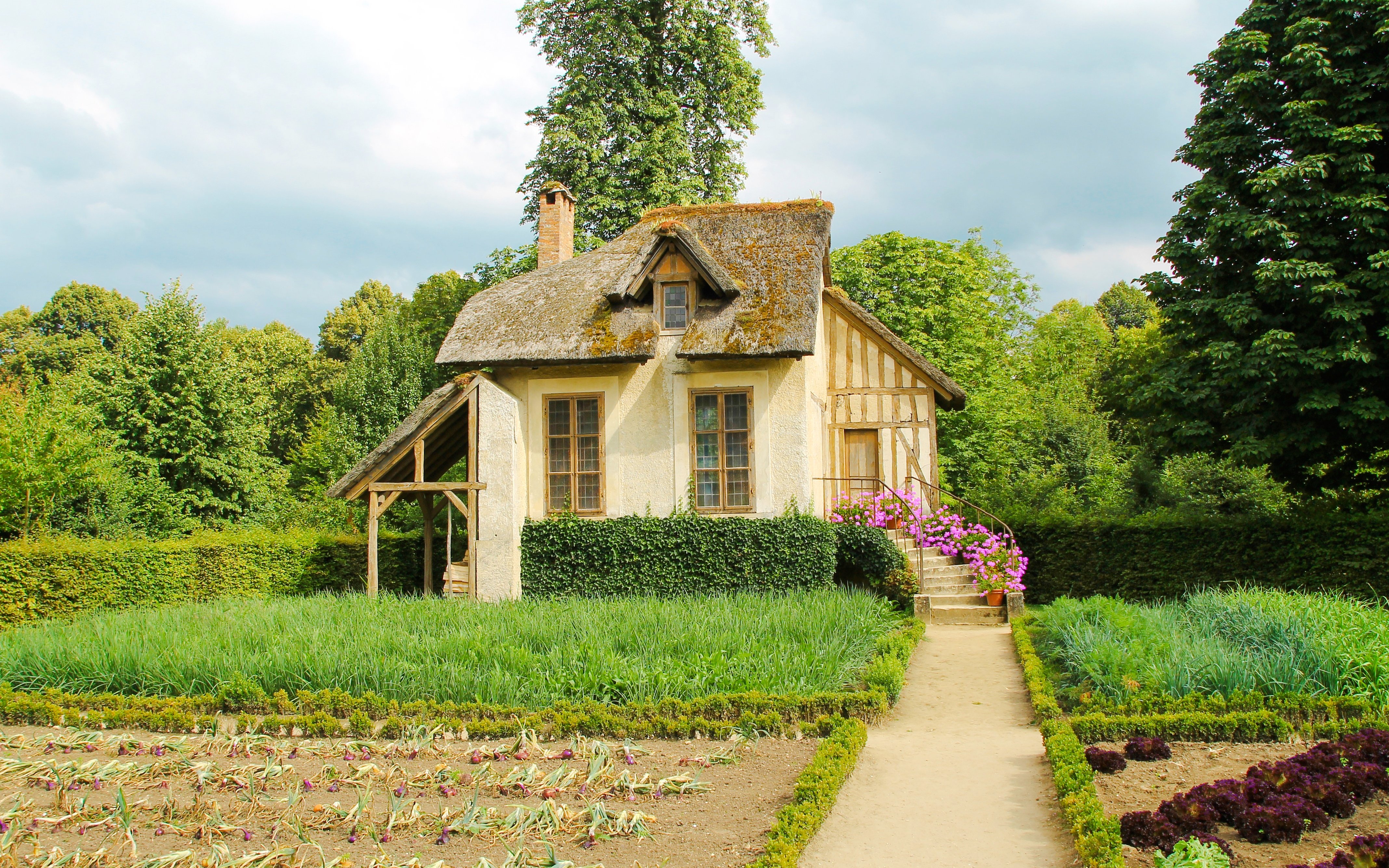 Cottage in Marie-Antoinette’s Hamlet, Versailles Gardens, surrounded by lush greenery and flower beds.