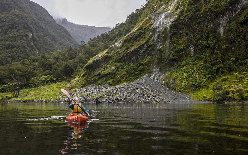Kayaker on Doubtful Sound fjord with lush cliffs, Te Anau overnight tour.